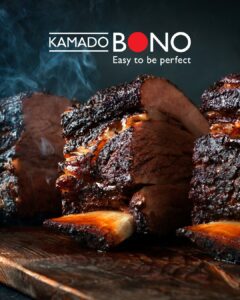 Smoked beef ribs sliced on a wooden board with Kamado Bono logo and slogan “Easy to be perfect” in the background